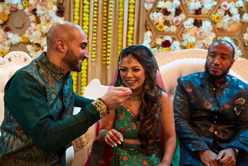 Guest feeding the bride a sweet as the groom sits beside her on the sofa
