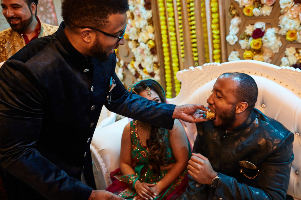 Guest leaning in to feed the groom a sweet