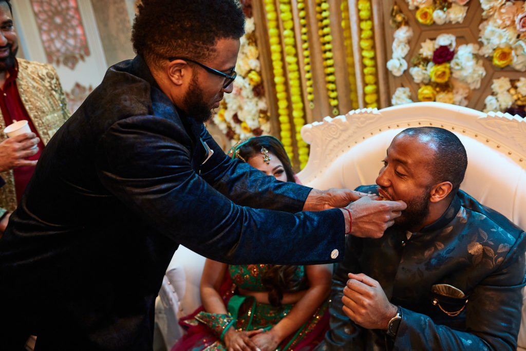 Guest feeding the groom a sweet as the bride laughs