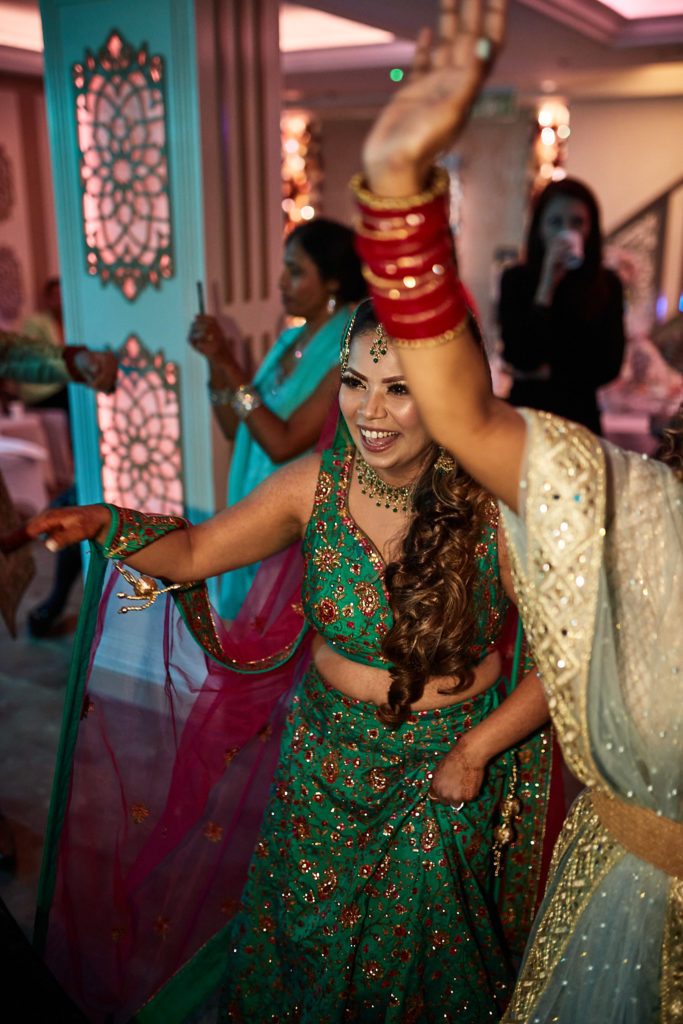 Bride dancing in her green lehenga with her arm in the air