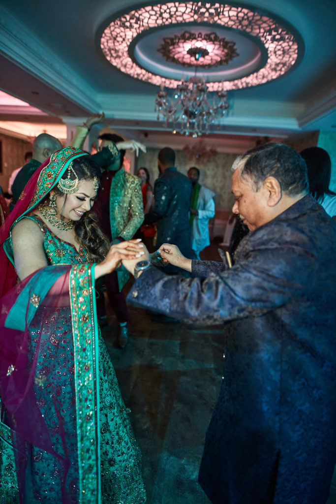 Bride in a green lehenga dancing with a guest under a chandelier
