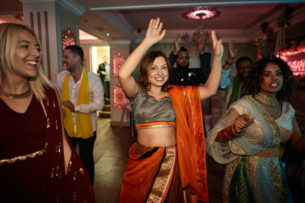 Guests dancing together, one in an orange sari
