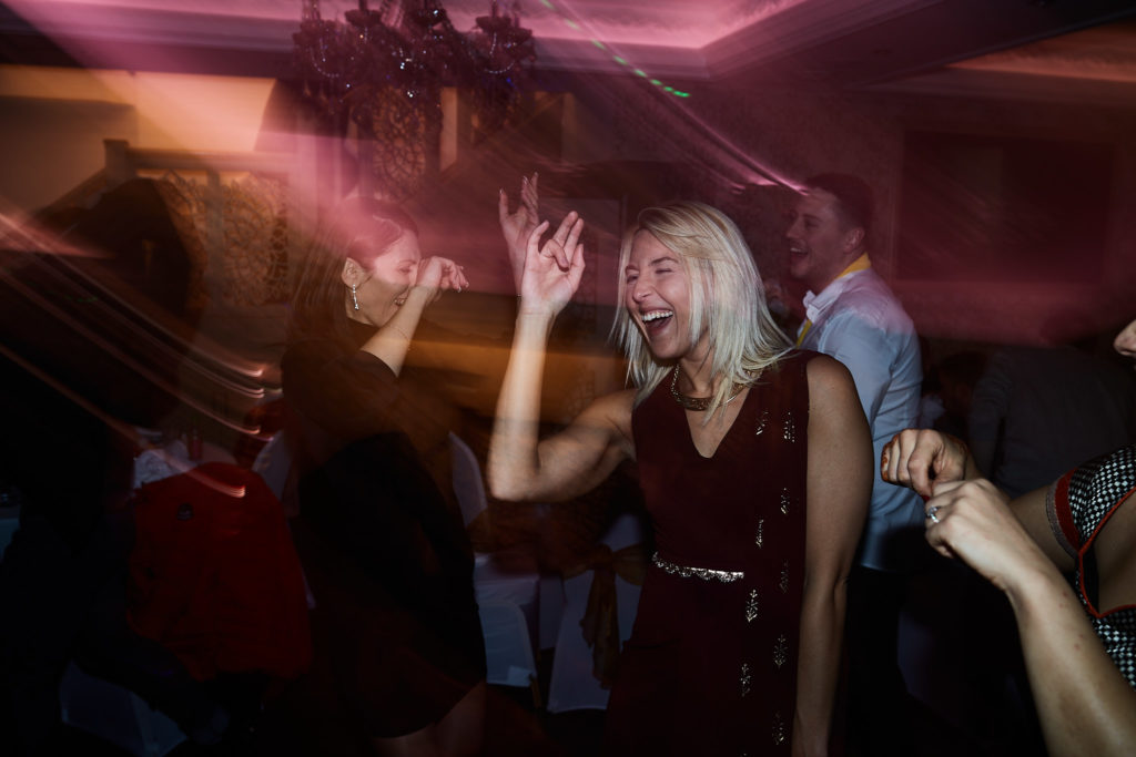 Guests dancing with their arms raised under pink lights