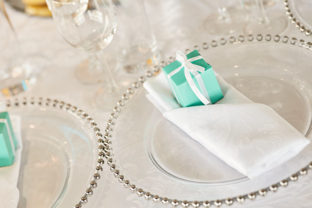 Place setting with a beaded glass charger and a turquoise favour box at a 60th birthday party