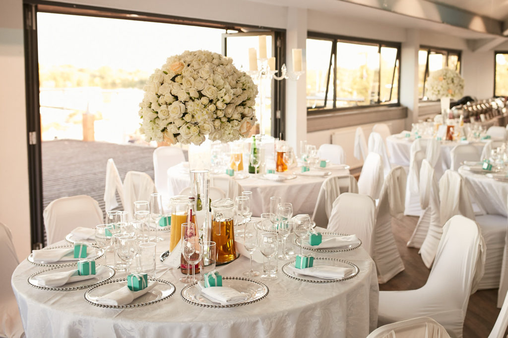 Round table with a centrepiece of cream roses beside the windows at Fairlop Waters