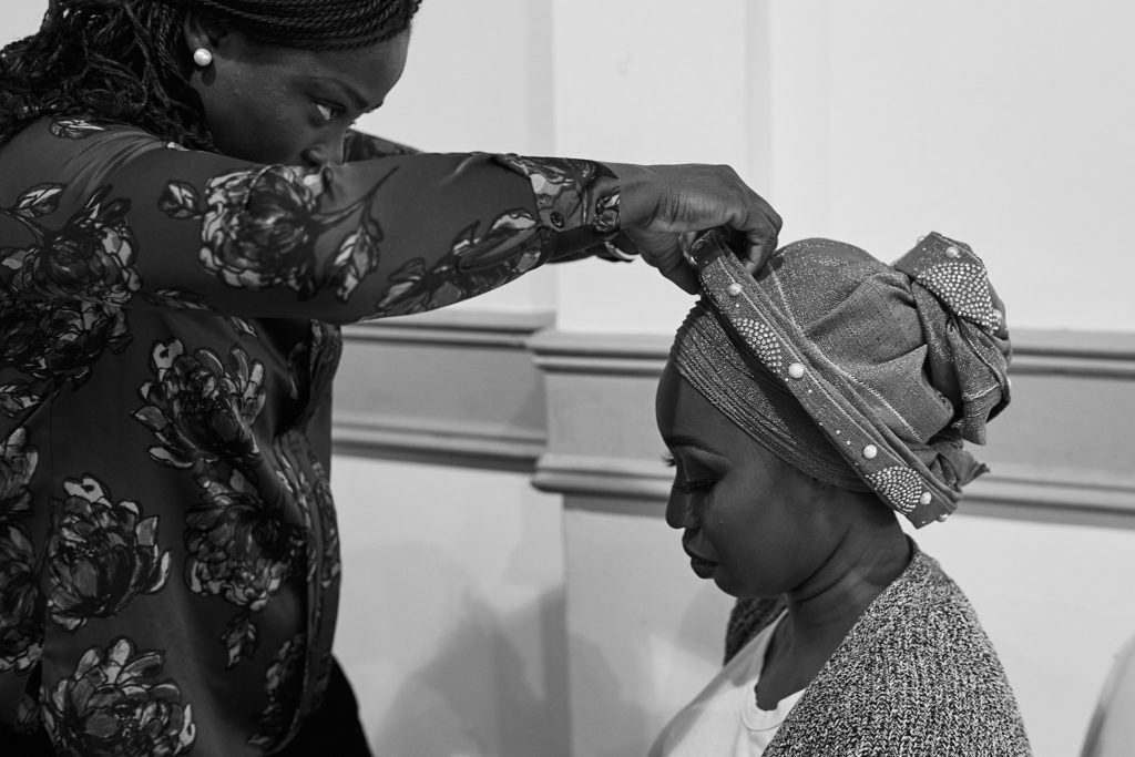 Black and white photo of a woman having her head tie adjusted before the party