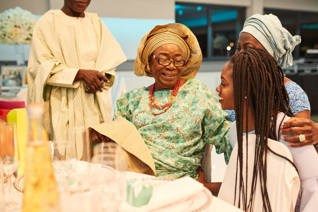 Guest in a green lace outfit and orange head tie smiling at the table