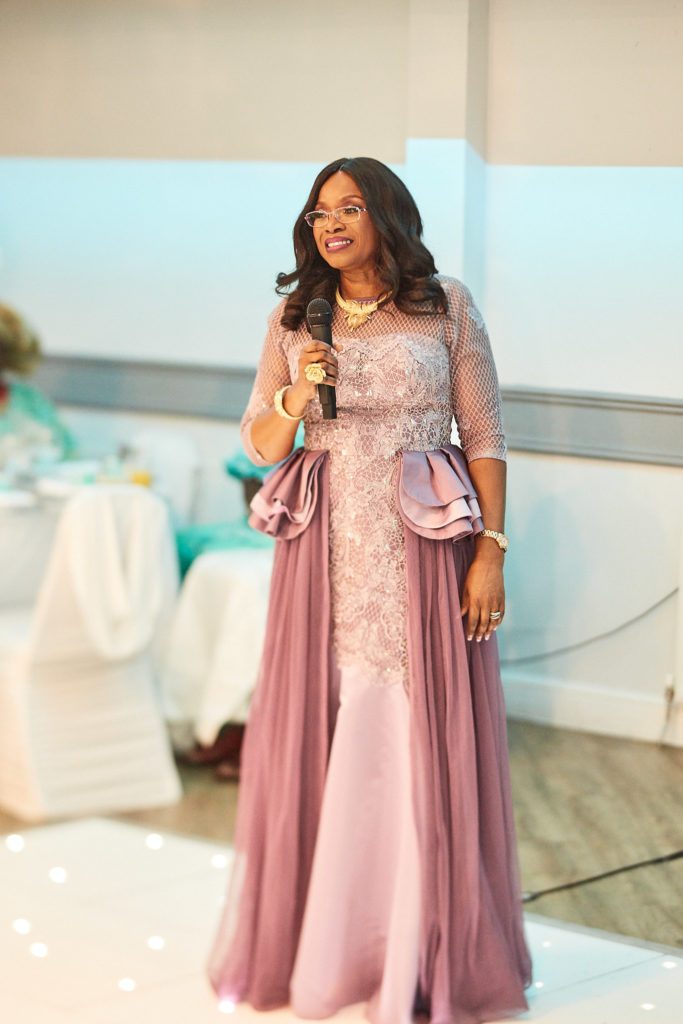 Host in a pink gown speaking with a microphone on the dance floor