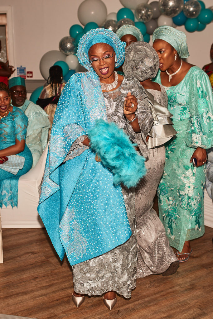 Guest of honour dancing with a turquoise feather fan beside guests in matching outfits
