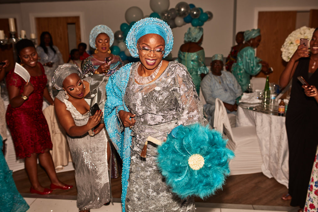 Guest of honour in turquoise and silver dancing with a feather fan as guests watch