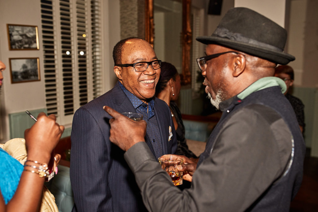 Two men laughing together at the party, one in a trilby hat