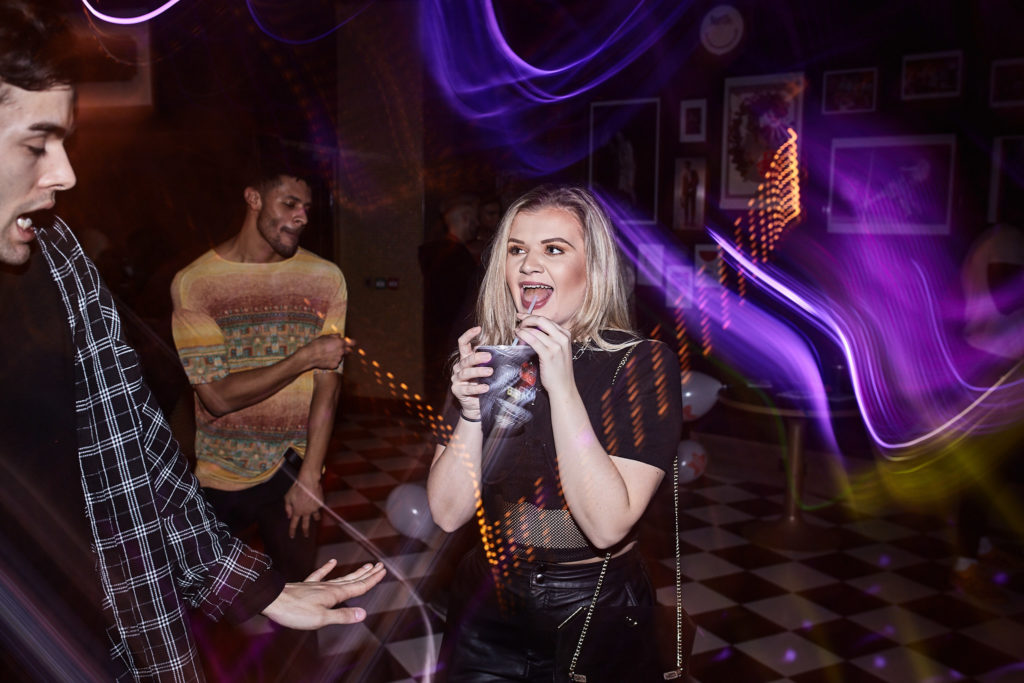 Guest laughing with a drink among streaks of purple light