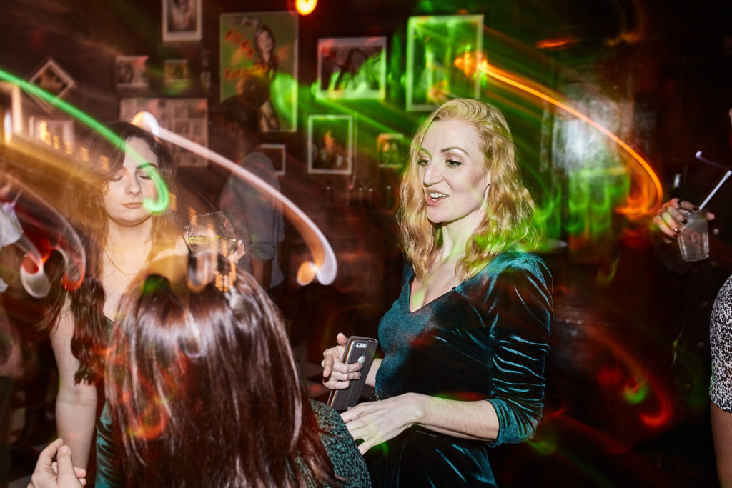 Guest in a velvet dress smiling among swirls of green and orange light