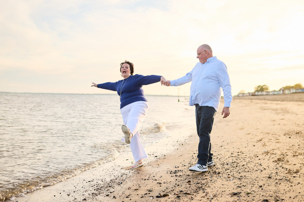 Engaged couple skipping hand in hand along the shoreline