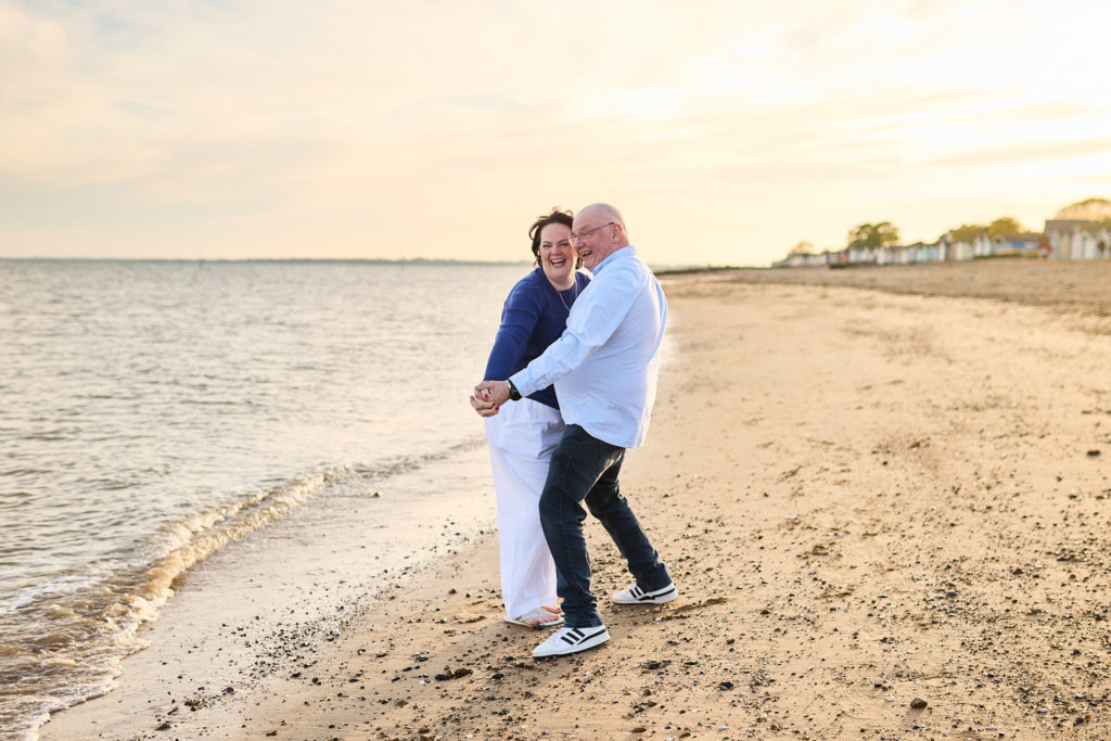 Engaged couple laughing as they walk arm in arm along the beach