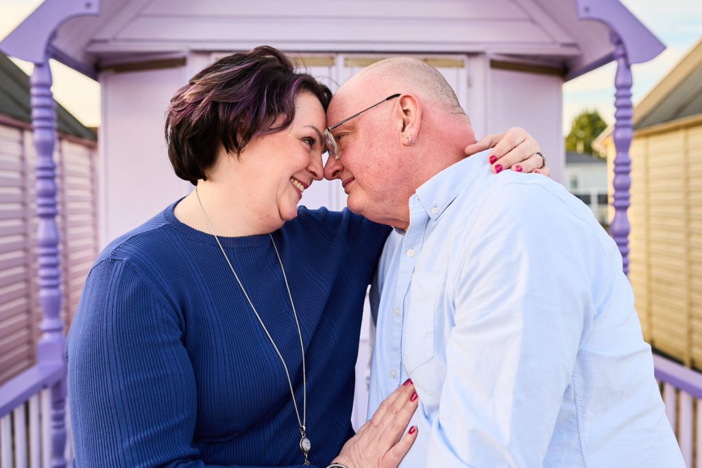 Engaged couple forehead to forehead on the porch of a lilac beach hut