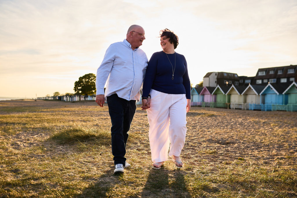 Engaged couple walking hand in hand along the shingle beach in evening light