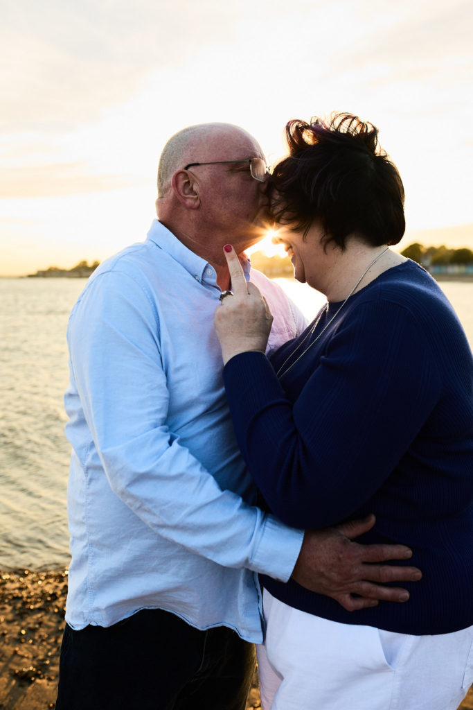 Engaged couple embracing forehead to forehead as the sun sets behind them