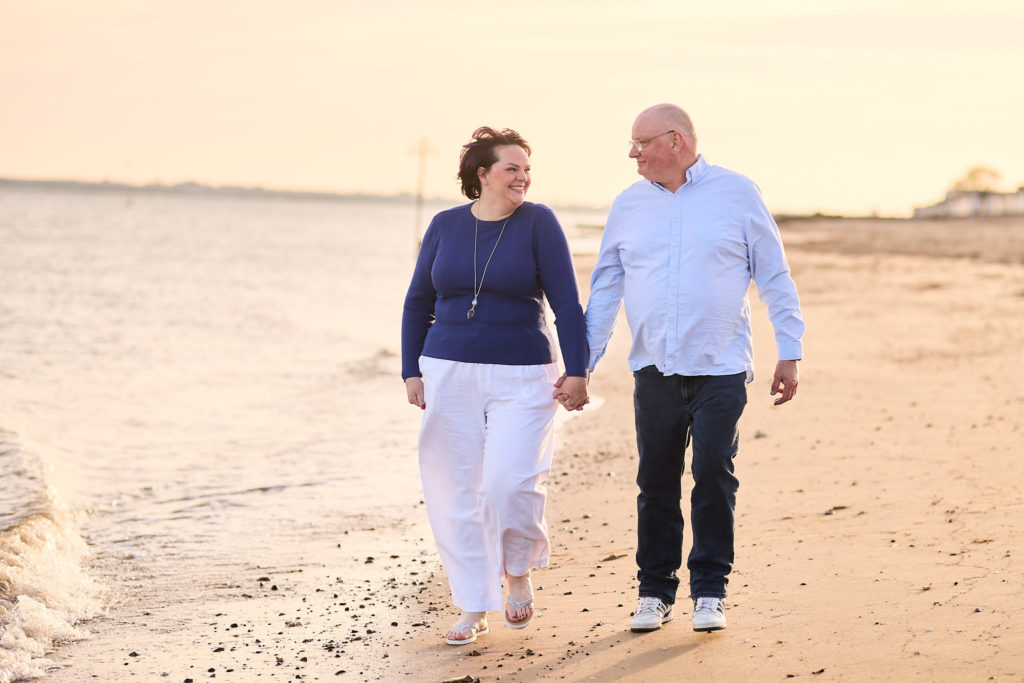 Engaged couple walking hand in hand along the sand at the water's edge
