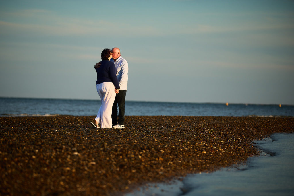 Engaged couple hugging on the shingle at dusk
