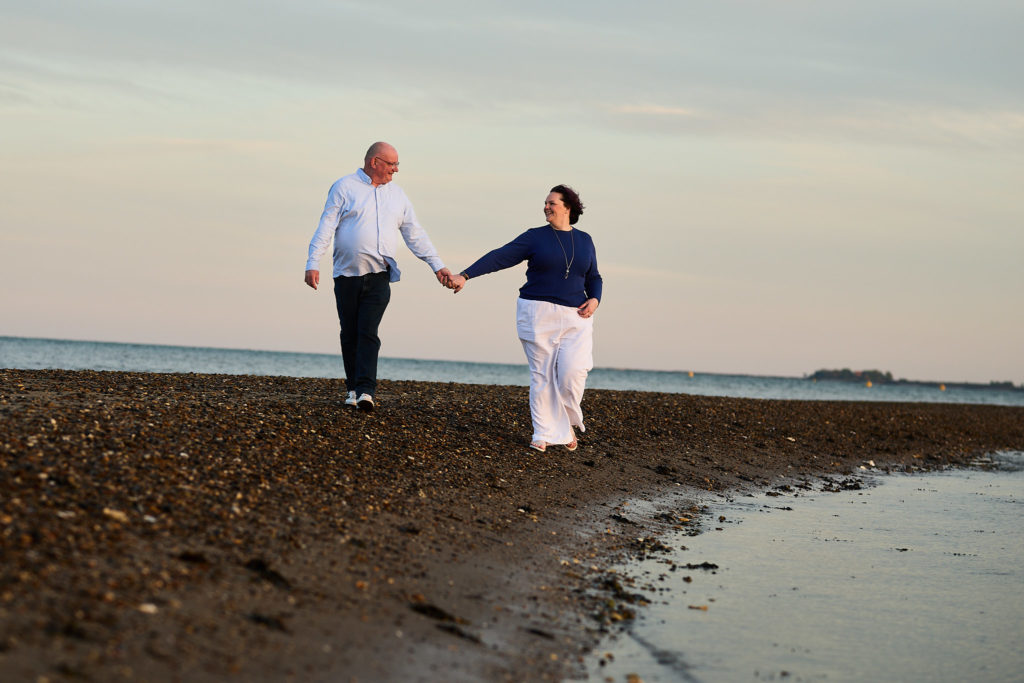 Engaged couple walking hand in hand along a shingle spit at dusk