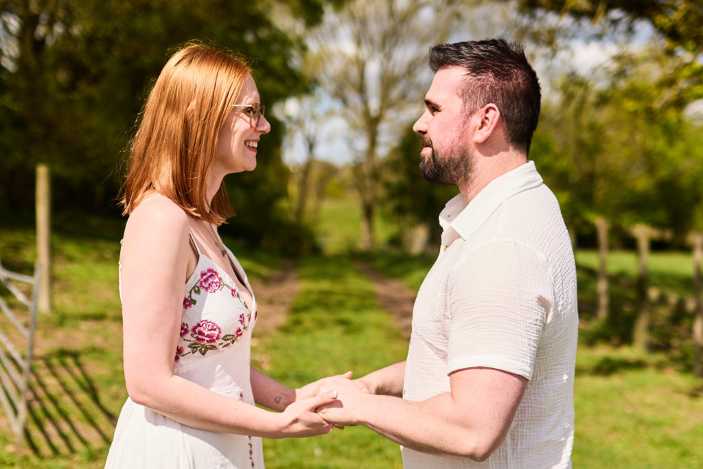Engaged couple holding hands and smiling at each other in a meadow