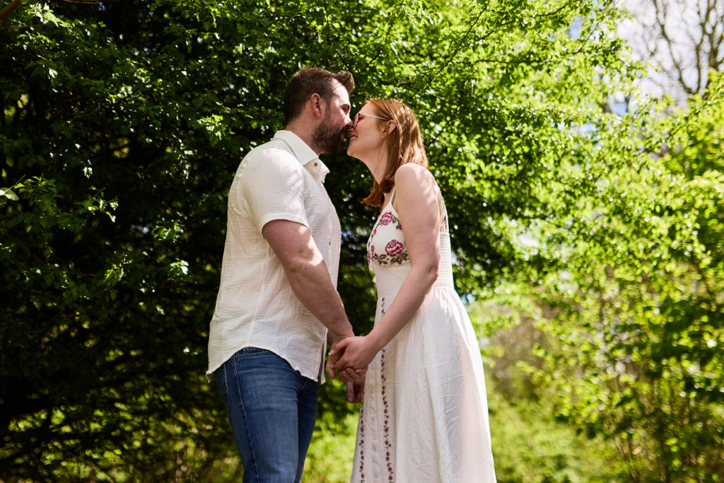 Engaged couple kissing in a leafy green wood