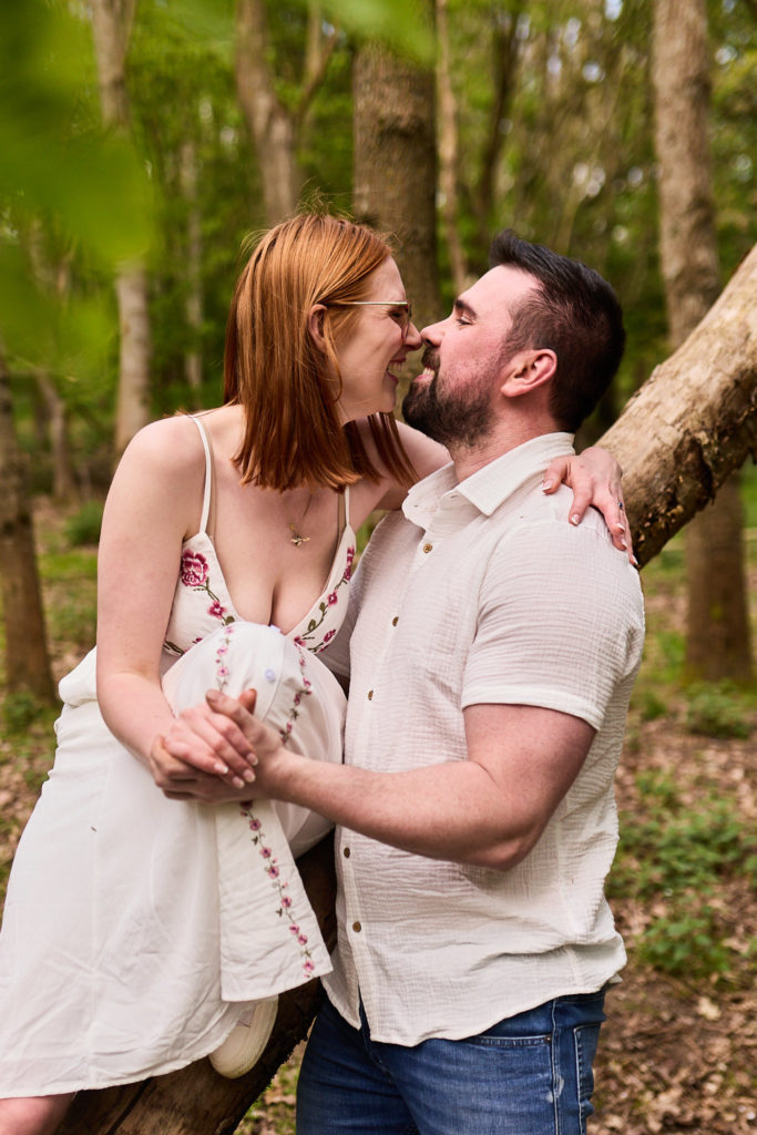 Engaged couple about to kiss beside a tree in the woods