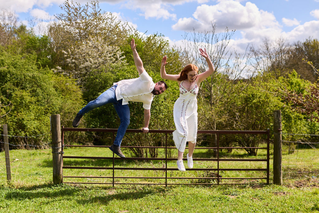 Engaged couple balancing along the top of a field gate