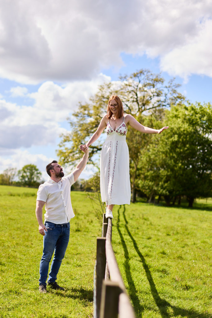 Woman balancing along a fence rail as her fiancé holds her hand