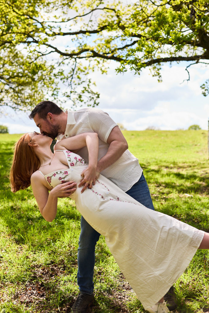 Man dipping his fiancée for a kiss beneath an oak tree