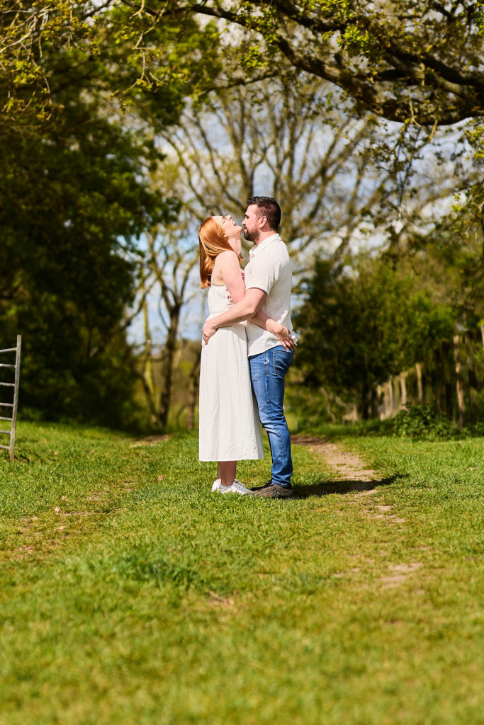 Engaged couple embracing on a grassy track beside the trees