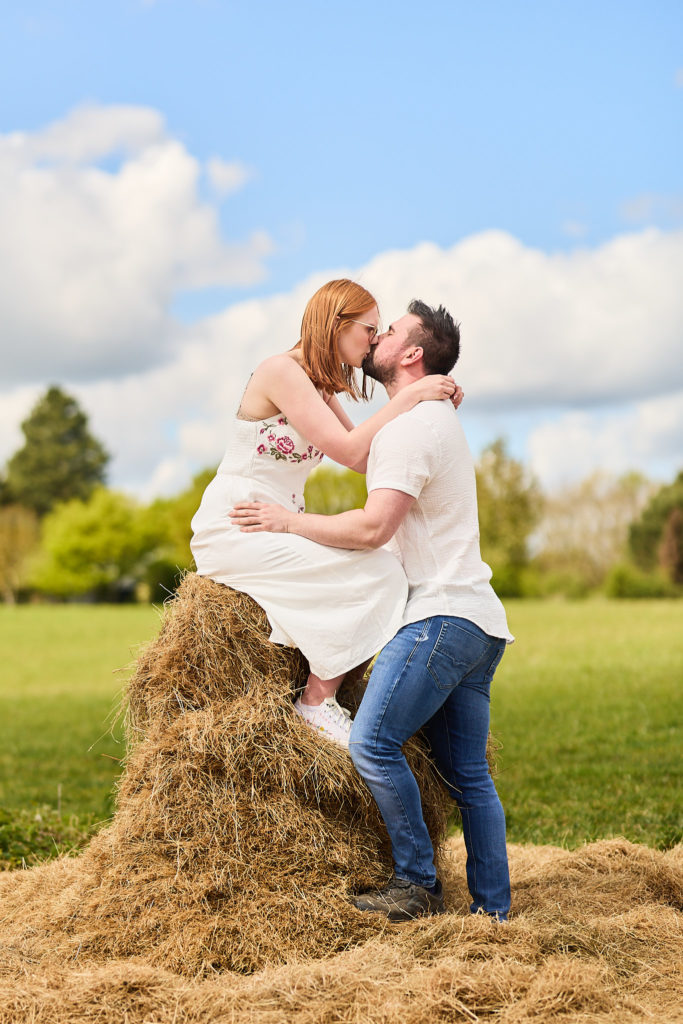 Woman sitting on a pile of hay kissing her fiancé
