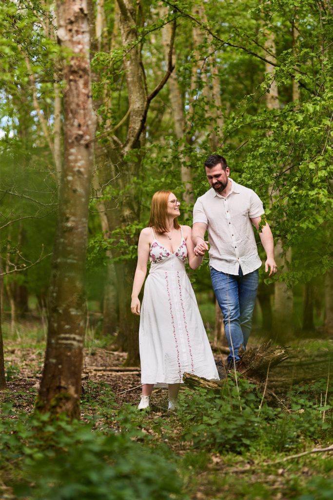 Engaged couple walking hand in hand through the woods on their relaxed Essex engagement shoot