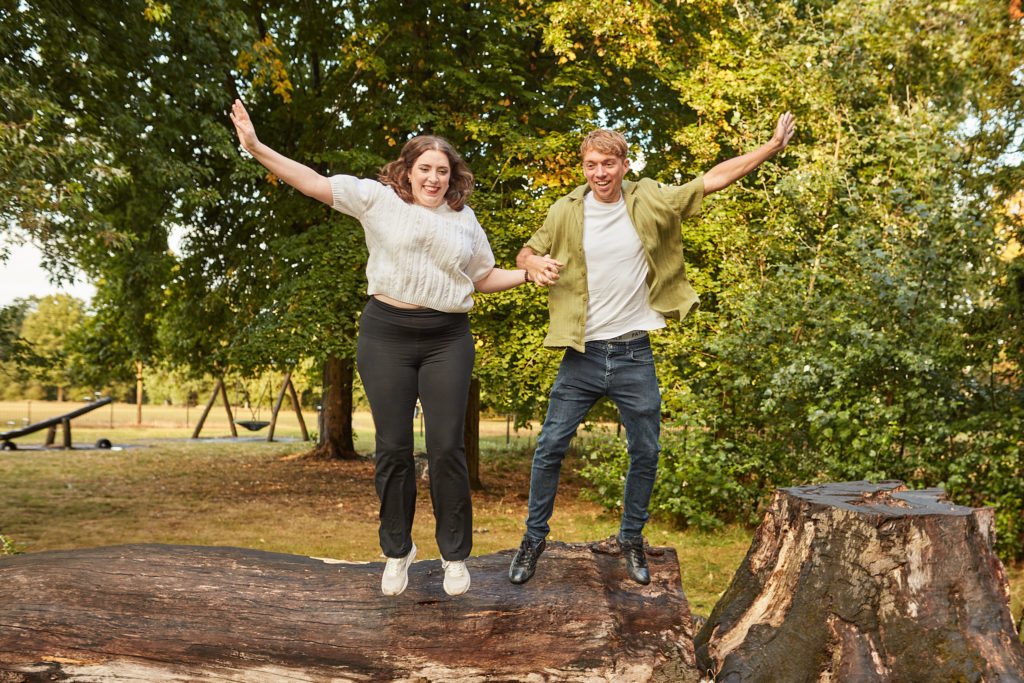 Engaged couple jumping off a tree stump with their arms in the air