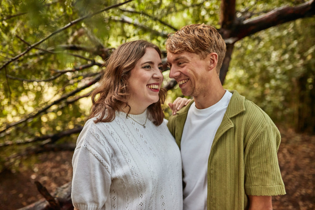 Woman laughing as her fiancé leans in close under pine branches