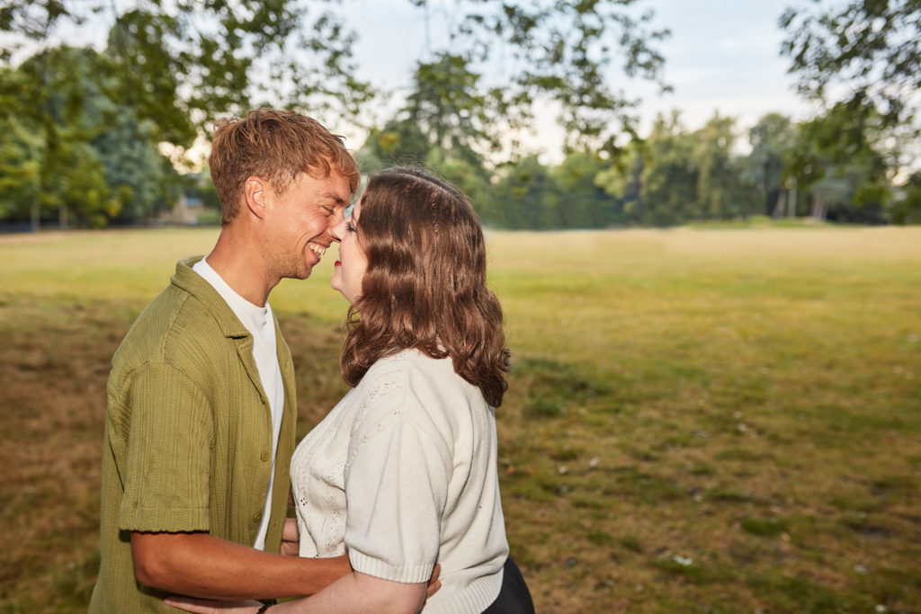 Engaged couple nose to nose and smiling in an open meadow at golden hour