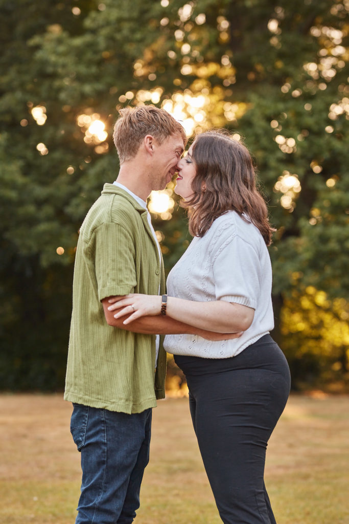 Engaged couple standing forehead to forehead with the sunset glowing through the trees in Chelmsford