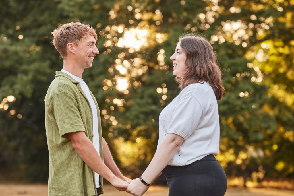 Engaged couple holding hands and smiling at each other at sunset on their engagement shoot in Chelmsford, Essex