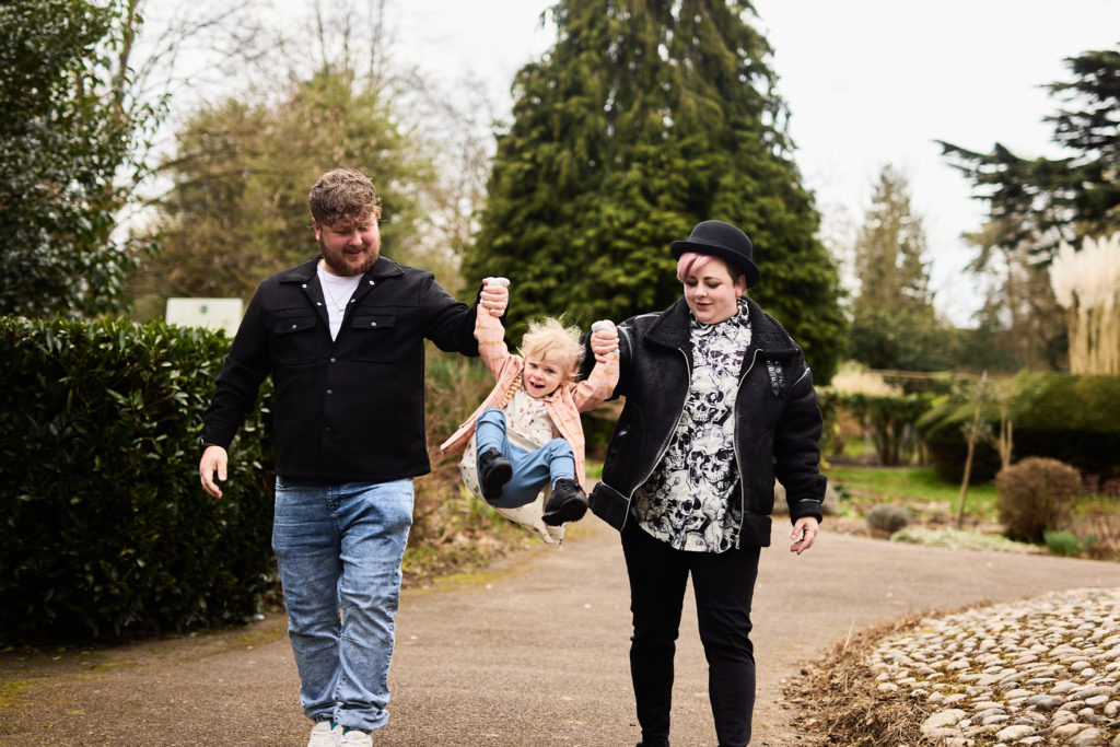 Couple swinging their toddler between them on a park path in Braintree