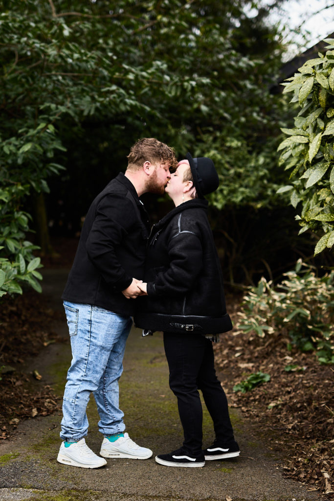 Engaged couple kissing on a path between the shrubs in a Braintree park
