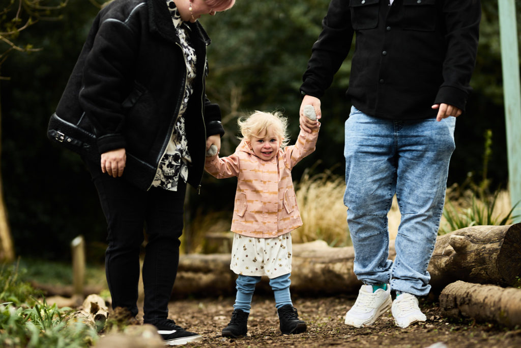 Toddler in a pink coat walking between her parents, holding both their hands