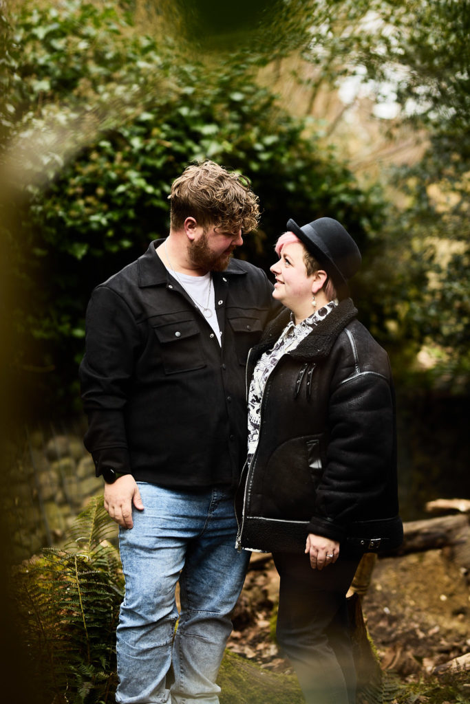 Engaged couple smiling at each other in matching black jackets in the park