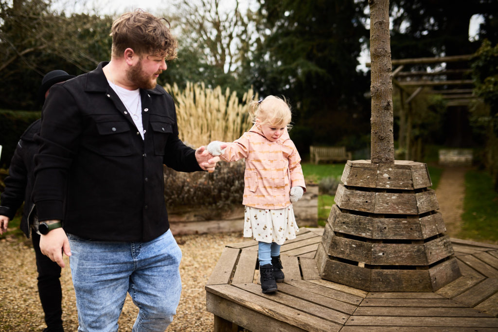 Man holding his toddler's hand beside a wooden tree seat in the park