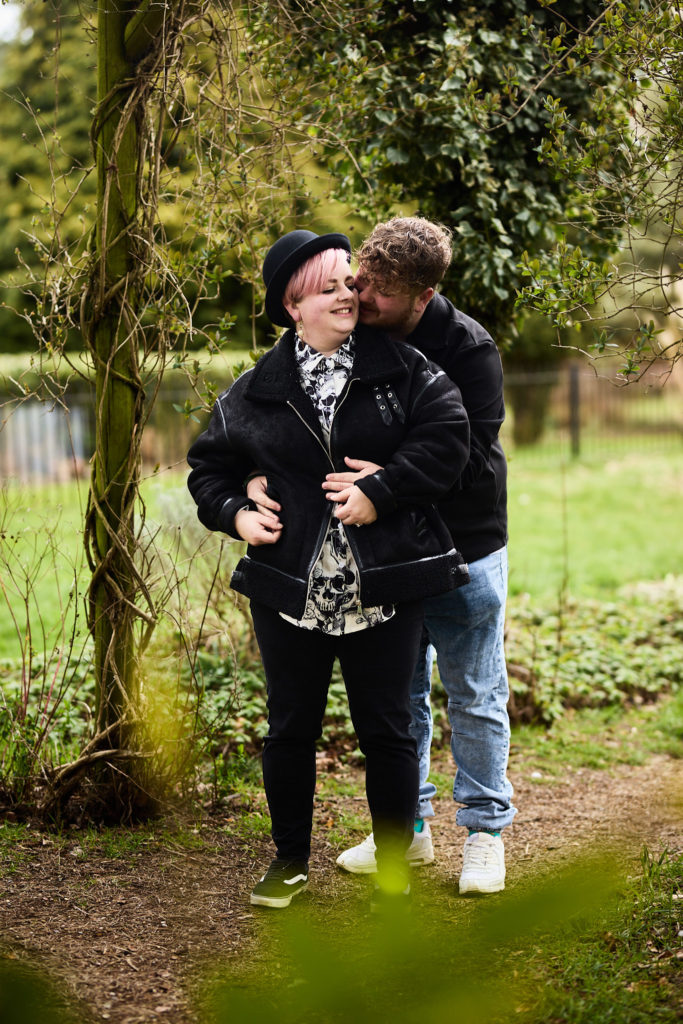 Man hugging his laughing fiancée from behind under a garden arch