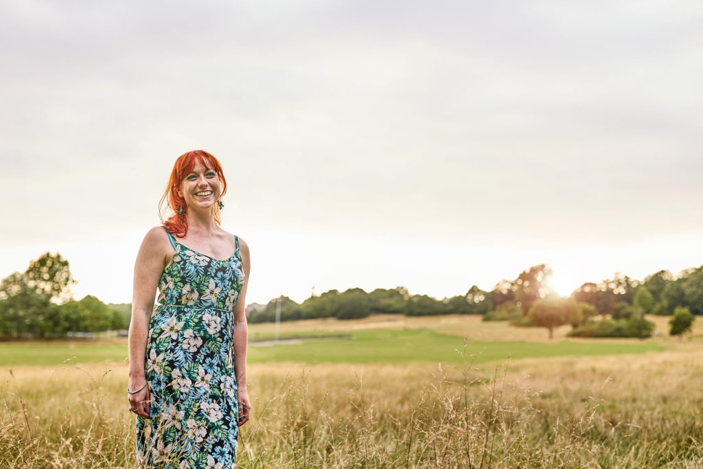 Woman with red hair standing in a meadow on Hampstead Heath in a floral dress
