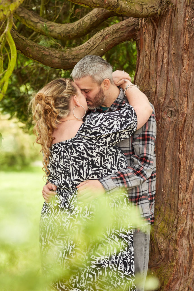 Engaged couple kissing beside a redwood tree in a Braintree park