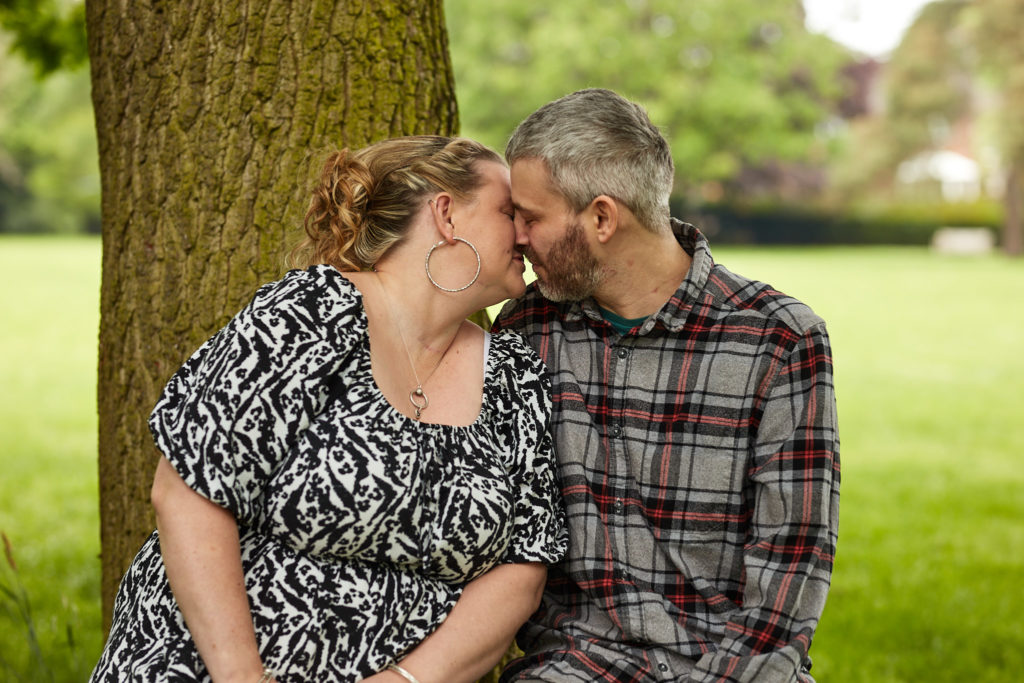Engaged couple sitting forehead to forehead at the foot of a tree