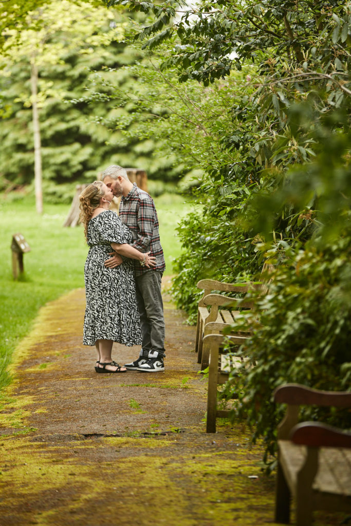 Engaged couple embracing on a mossy path between the trees