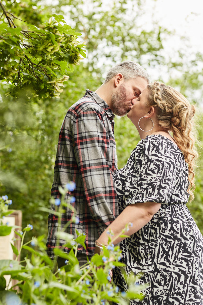 Engaged couple kissing among spring leaves in the park